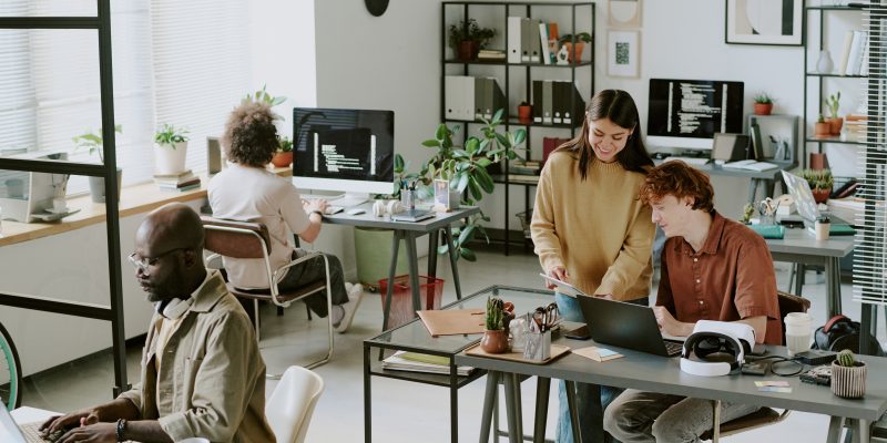 High angle shot of cozy office full of digital devices and furniture, biracial workers interacting with each other and working