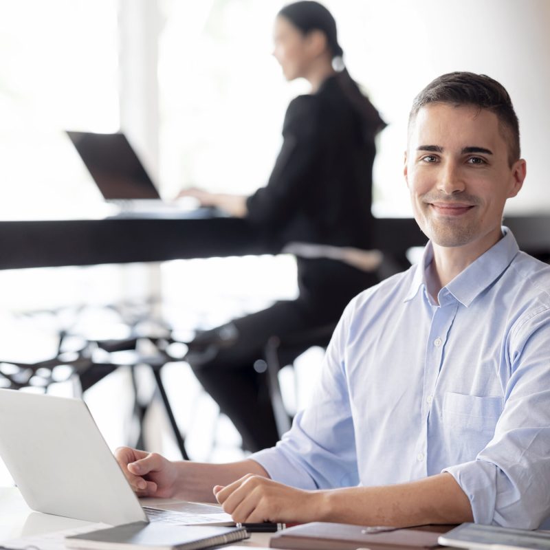 Portrait of happy concentrated businessman sitting at office desk, looking at camera, smiling.